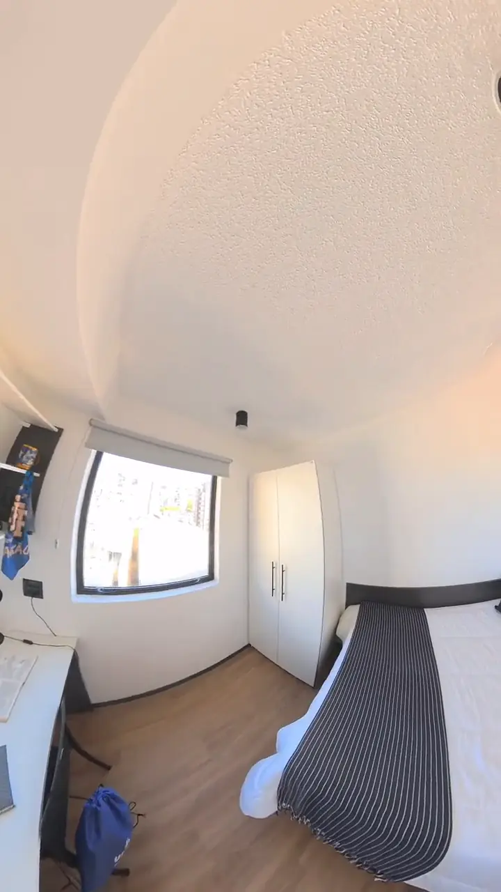 Studio mobiliado com cama de casal, janela ampla e piso de madeira, em vídeo 360º reenquadrado