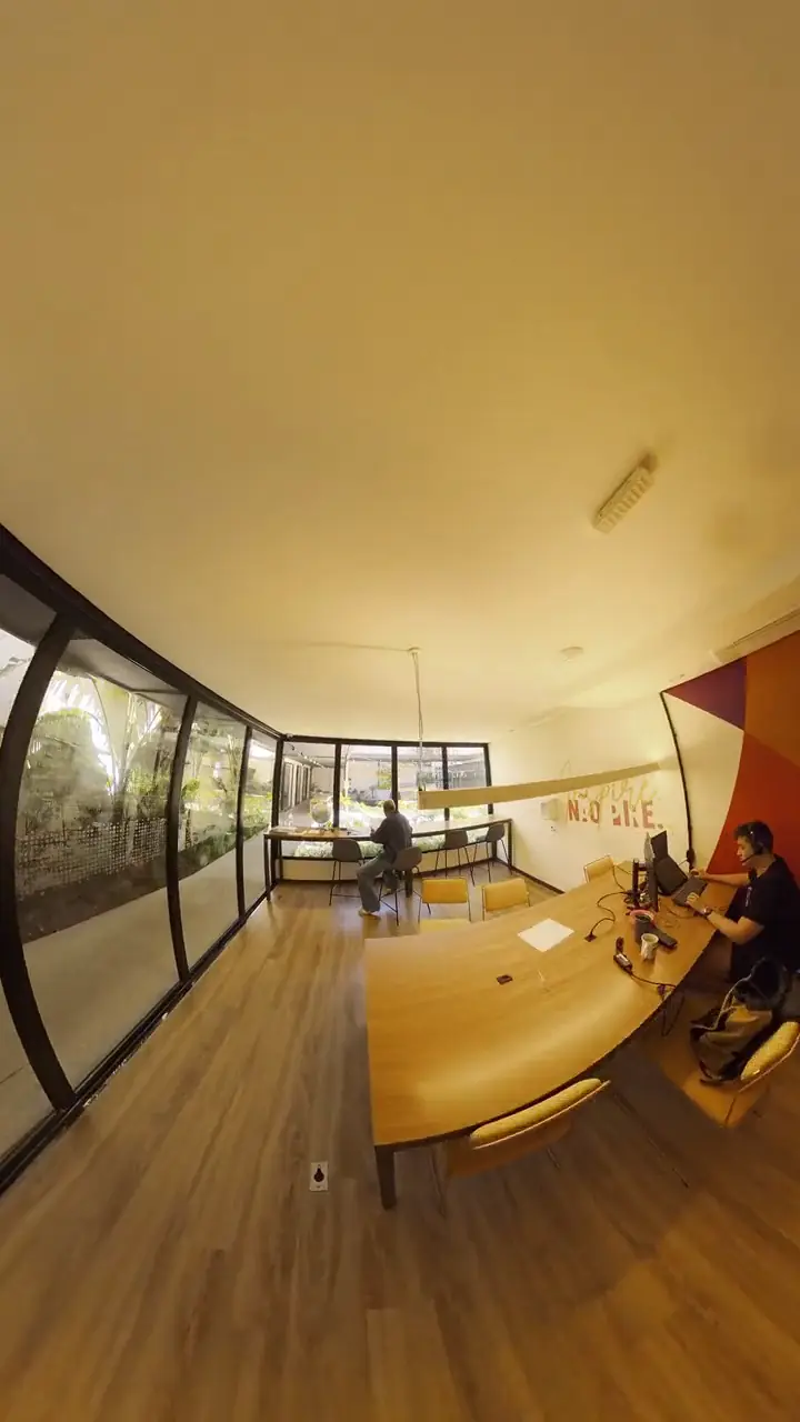 Coworking com mesas de madeira e fachada envidraçada para o jardim, em vídeo 360º reenquadrado
